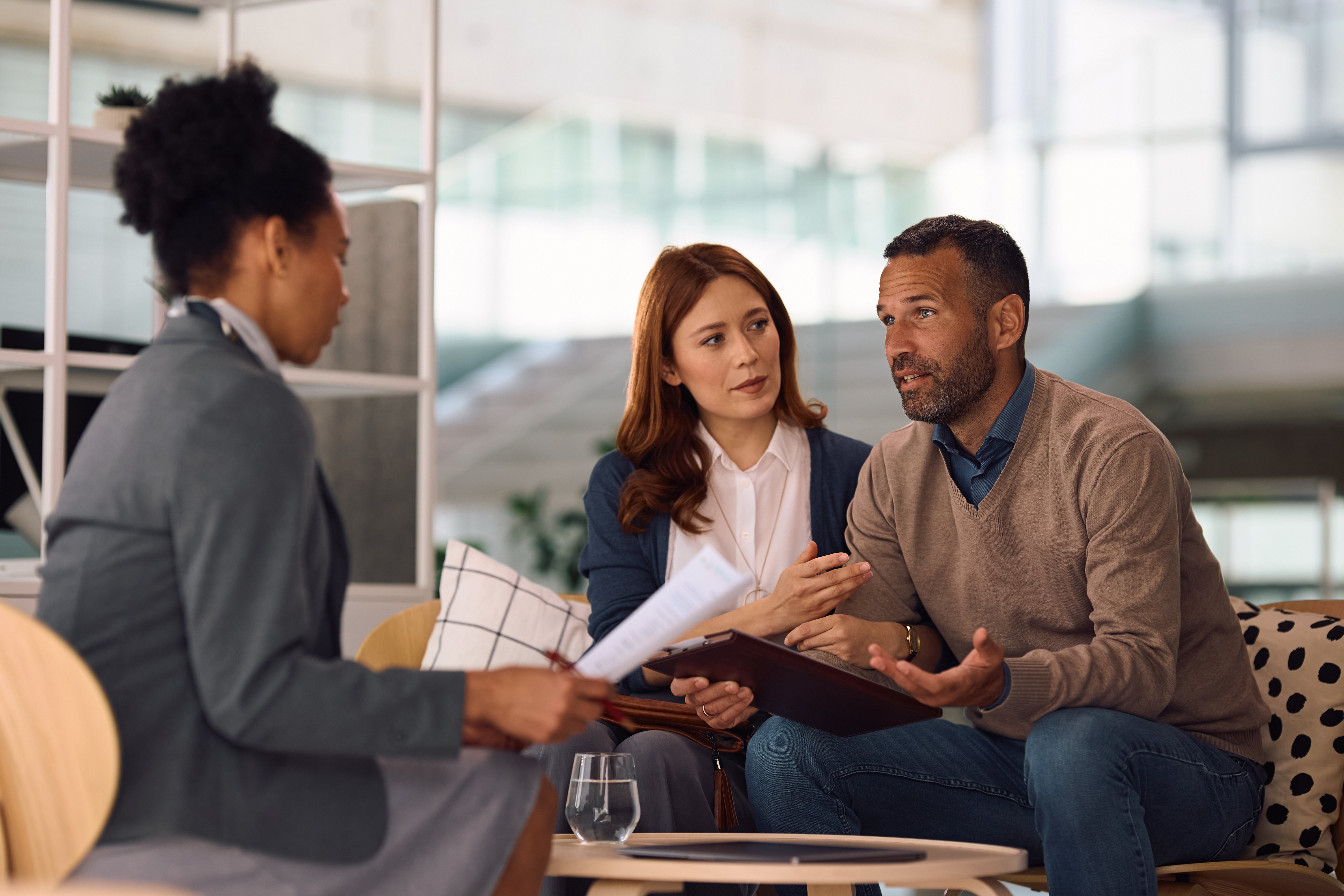 Mid adult couple communicating with insurance agent while going through their financial reports during the meeting.  Focus is on man.